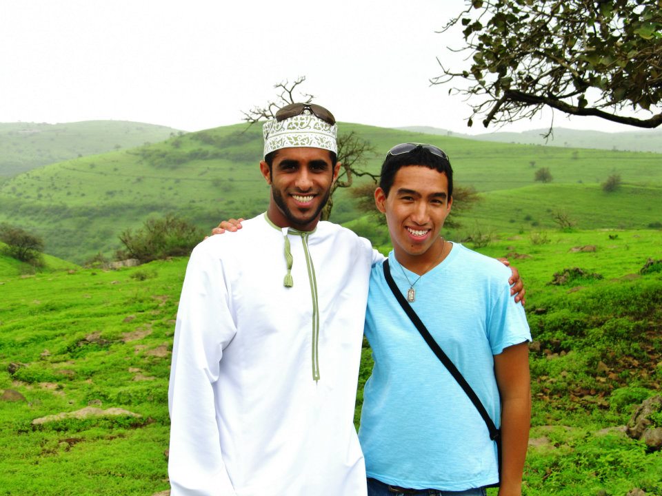 Carlo posing with a friend in Oman outdoors, in front a bright, green field.