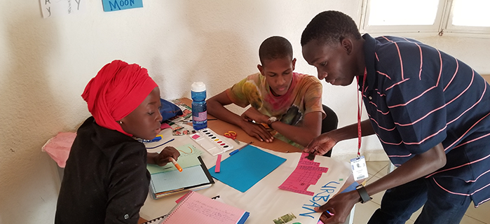 Moustapha (standing, right) helps students with a project during the English Workshop in Senegal