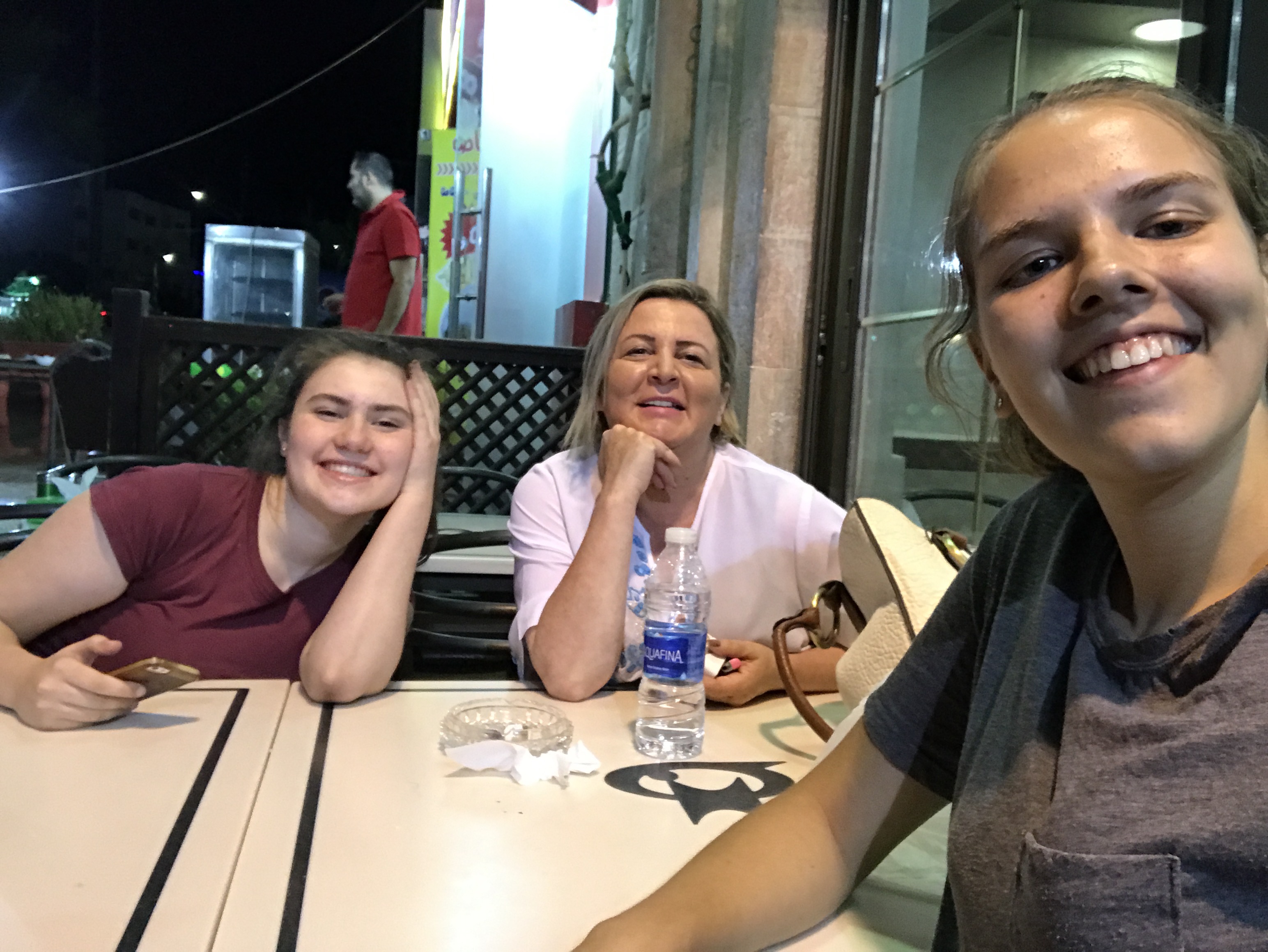 Phoebe smiles in this selfie shot, seated at an outdoor table with her host mom and another YES Abroad student.
