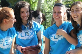 A group of young women wearing light blue FLEX T-shirts, laugh and smile at the camera