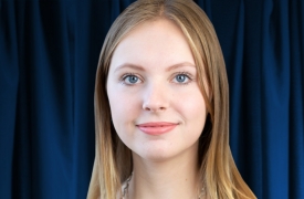 Headshot of Yulia, smiling with dark blue curtains behind her