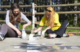 Two female alumni are painting outside as part of a community cleanup project