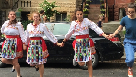 Hannah, wearing Converse sneakers and jeans, dances alongside three young Bulgarian girls wearing traditional folk costume