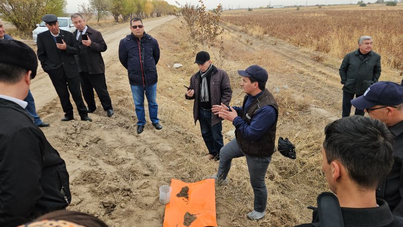 Man speaks to large group of individuals in a field with soil samples in front of him