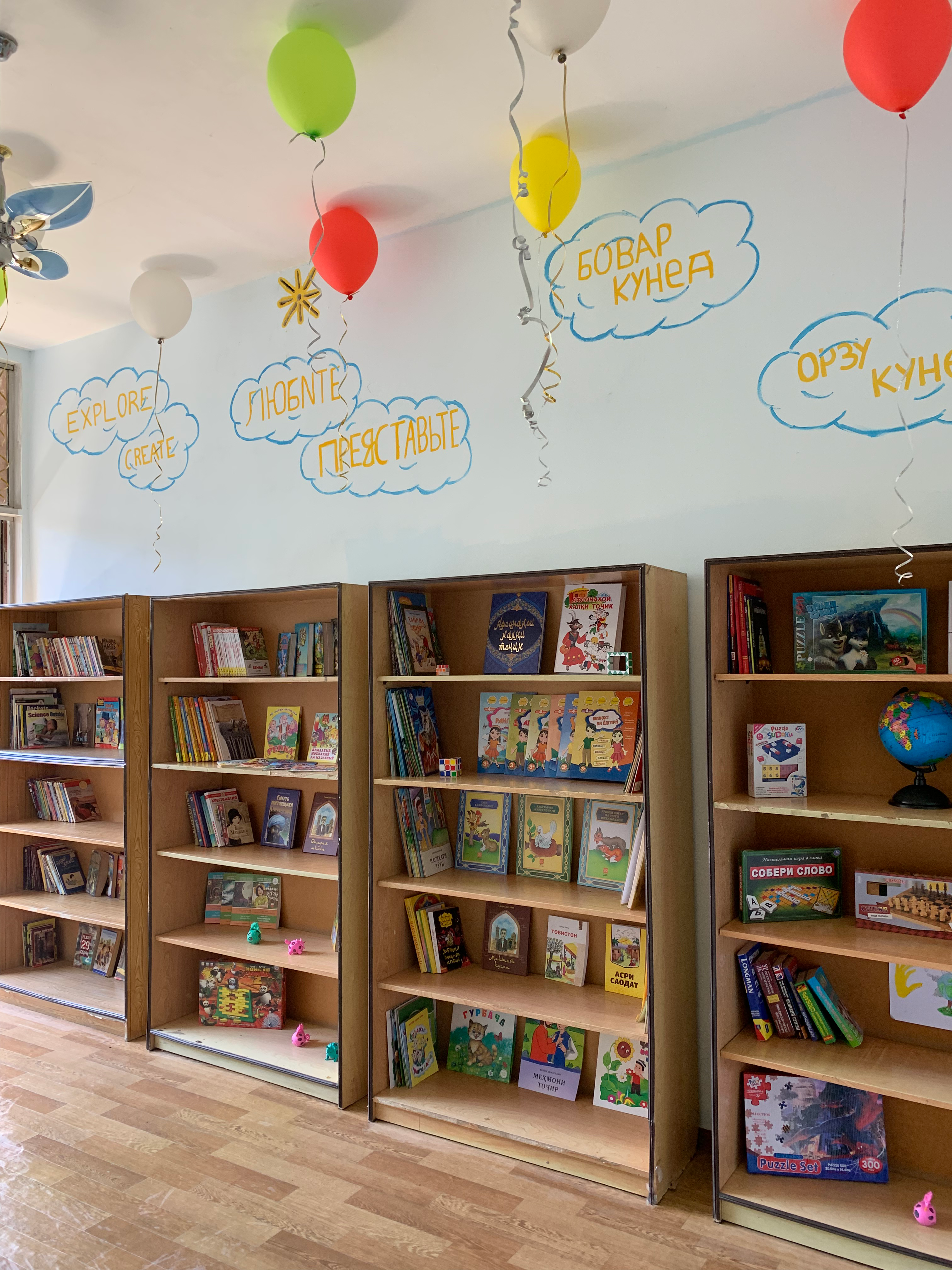 The finished library, with painted murals, books on shelves, and balloons hanging
