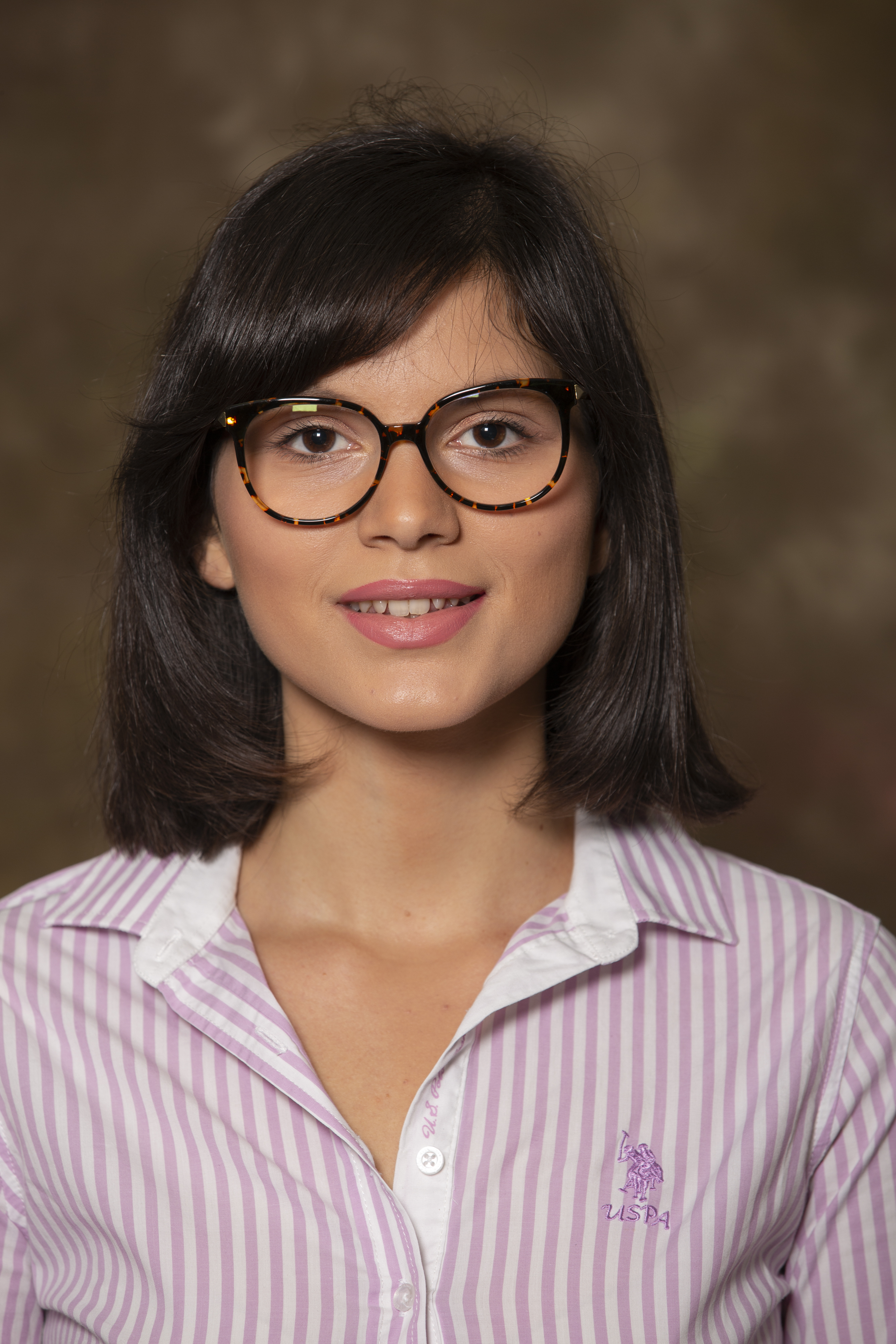 Headshot of Hana, smiling at the camera, wearing red glasses