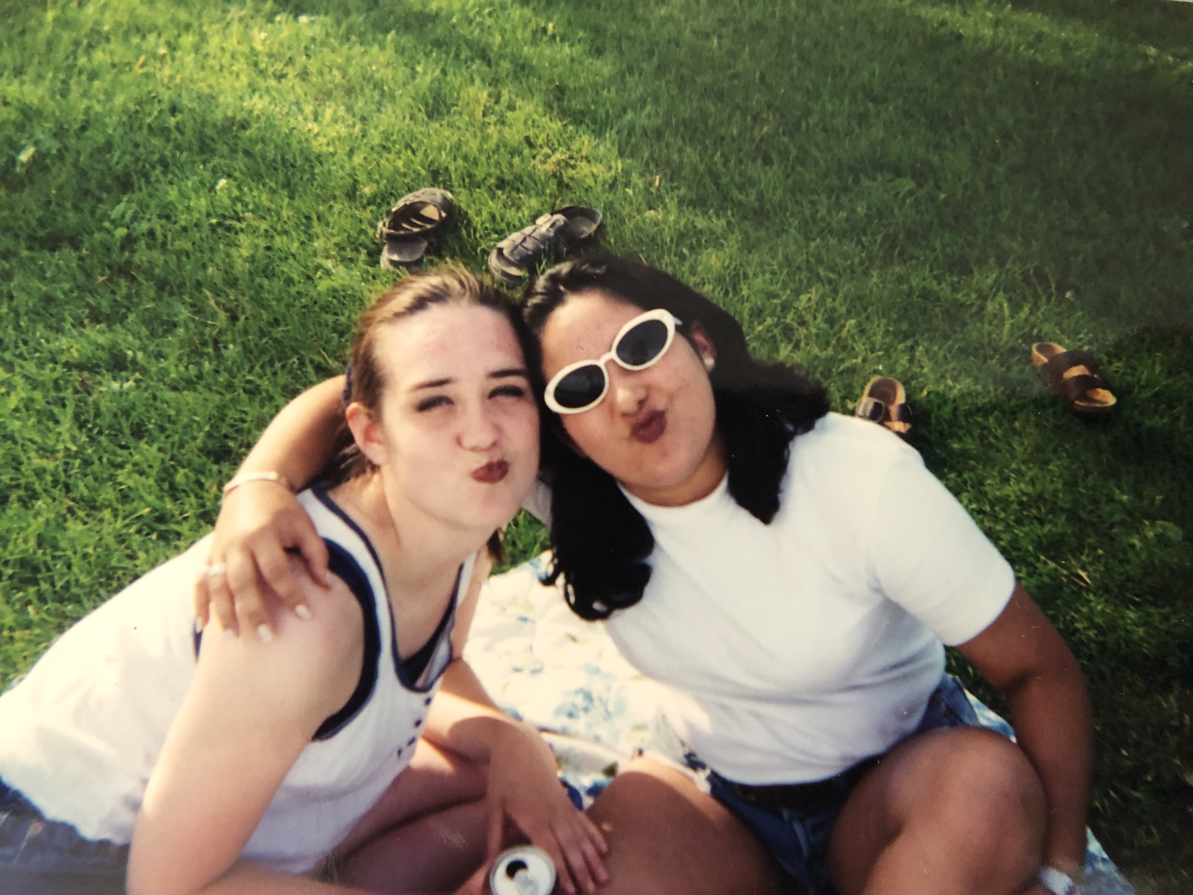 A teenaged Karissa and host sister making kissy faces, arm in arm, sitting on a picnic blanket together