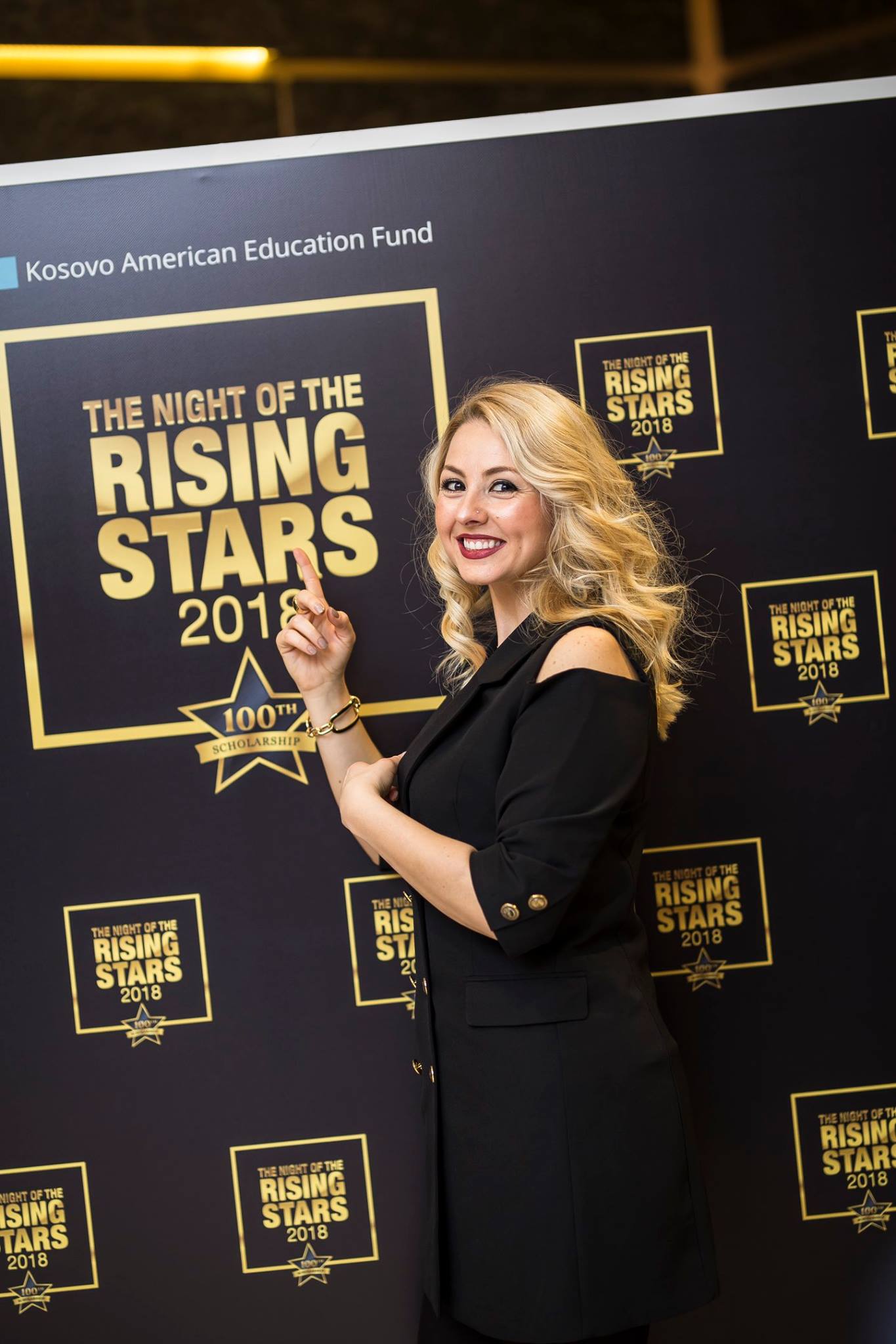 A woman at the KAEF dinner smiles and poses in front of a backdrop that reads "Night of the Rising Stars"