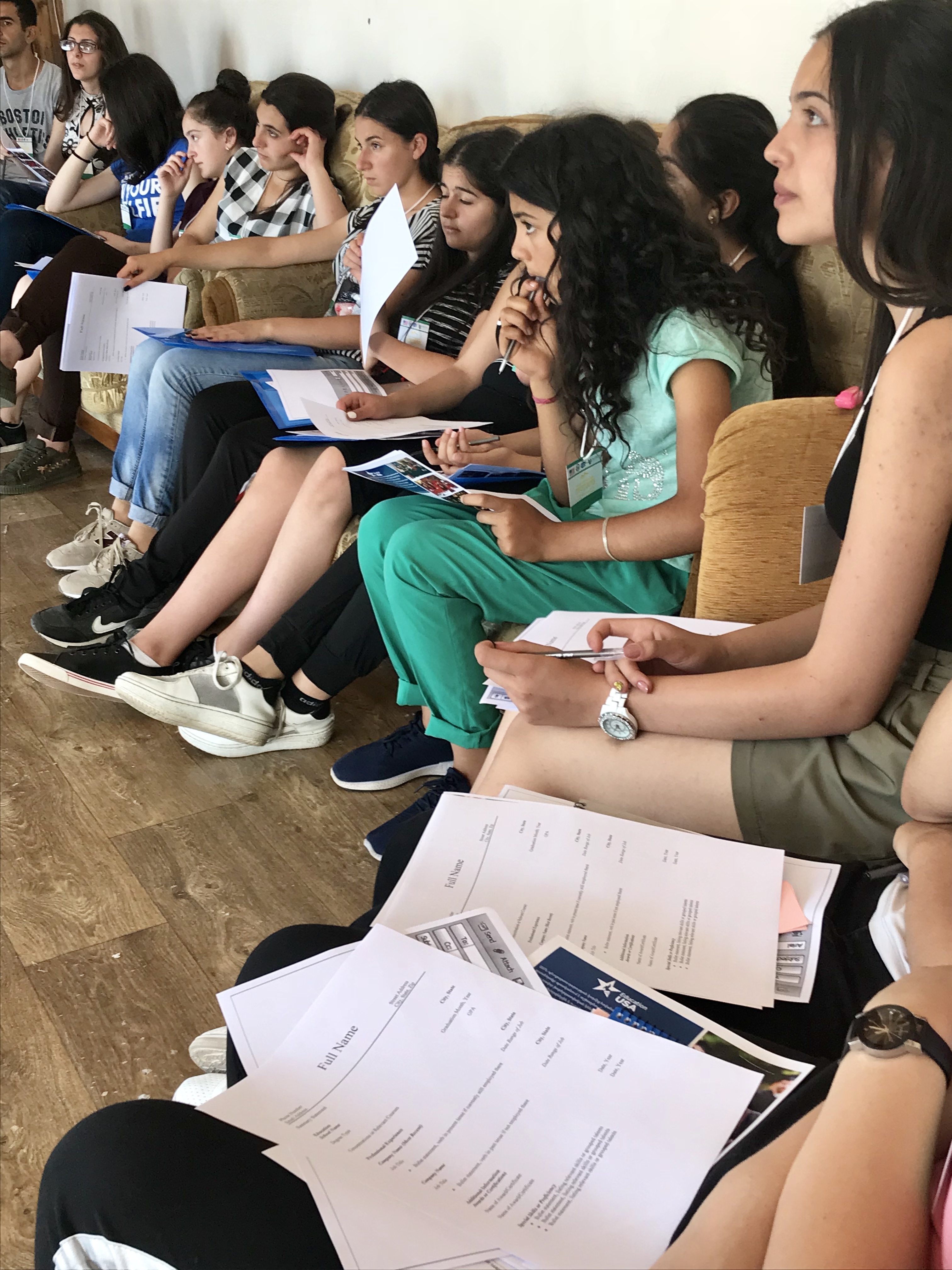 FLEX students sit in chairs along the edge of a room, writing and engaged in an activity