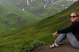 AC Study Abroad student Kay sits on a lush green hillside, nestled in the mountains