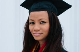 Raina, wearing a cap and gown, smiles at the camera in this portrait shot