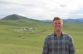 Chris smiles, standing in front of rolling green hills