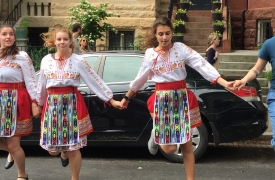 Hannah, wearing Converse sneakers and jeans, dances alongside three young Bulgarian girls wearing traditional folk costume