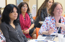 Several educators seated around a table, listening to a presenter