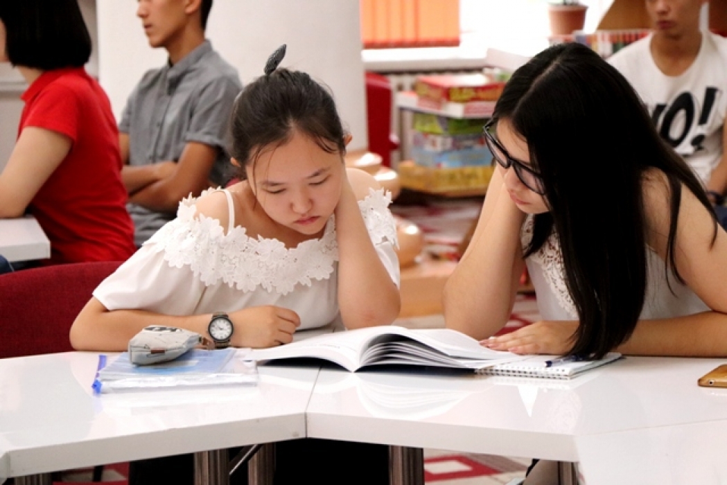Two young women share a book while studying 