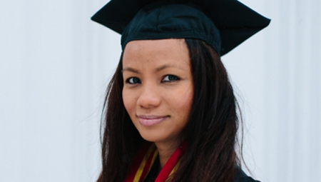 Raina, wearing a cap and gown, smiles at the camera in this portrait shot