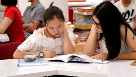 Two young women share a book while studying