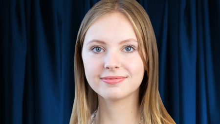 Headshot of Yulia, smiling with dark blue curtains behind her