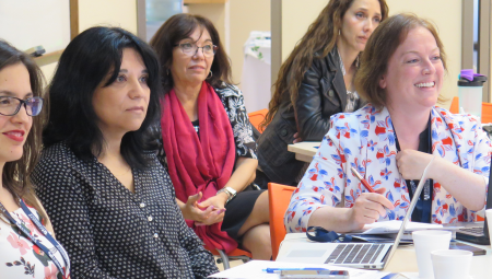 Several educators seated around a table, listening to a presenter