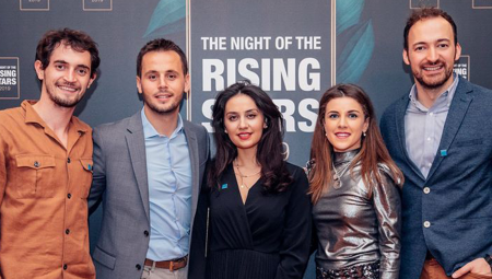 Several attendees, dressed to impress, in front of the step and repeat wall at the event