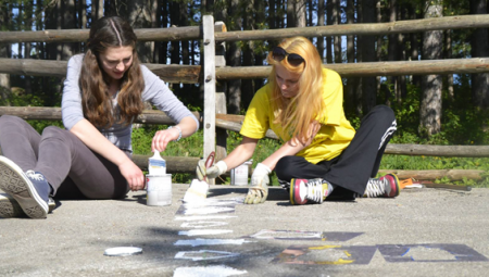Two female alumni are painting outside as part of a community cleanup project