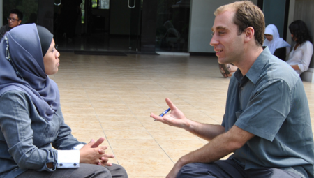 Two language partners converse while sitting on the ground